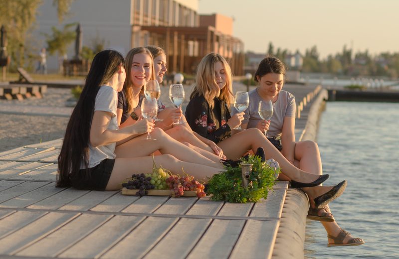 Friends sharing wine and food by the water at sunset